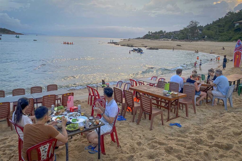 Casual beach dining at Bai Xep Beach – Visitors enjoying fresh seafood and cold beers at simple seaside tables as the sun sets over the bay.