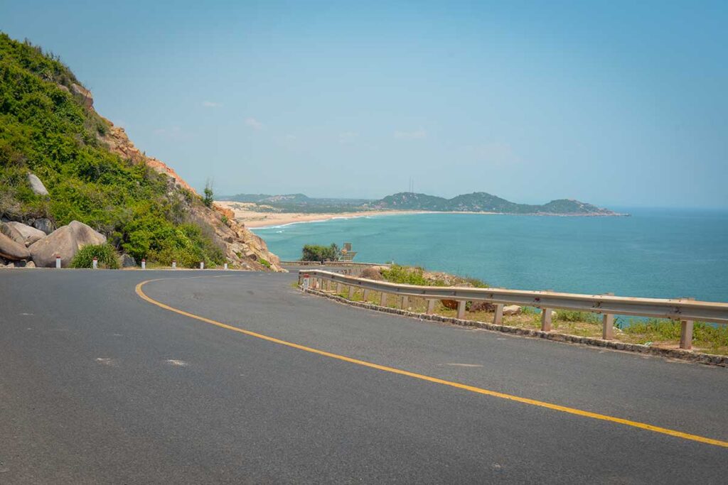 Scenic coastal road between Quy Nhon and Phu Yen with sweeping views of turquoise sea and golden sandy beaches below the hillside.