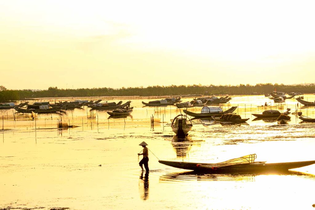 A man dragging his small fishing boat with a rope during sunset at Tam Giang Lagoon