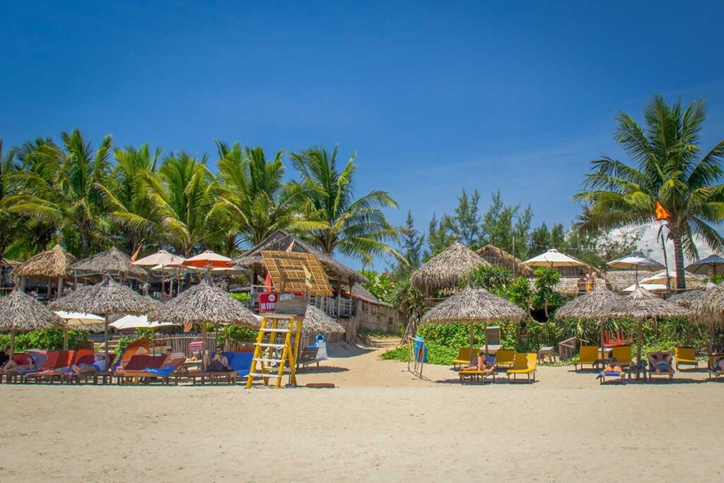 Colorful beach bars and palm trees lining the sandy shore of An Bang Beach in Hoi An