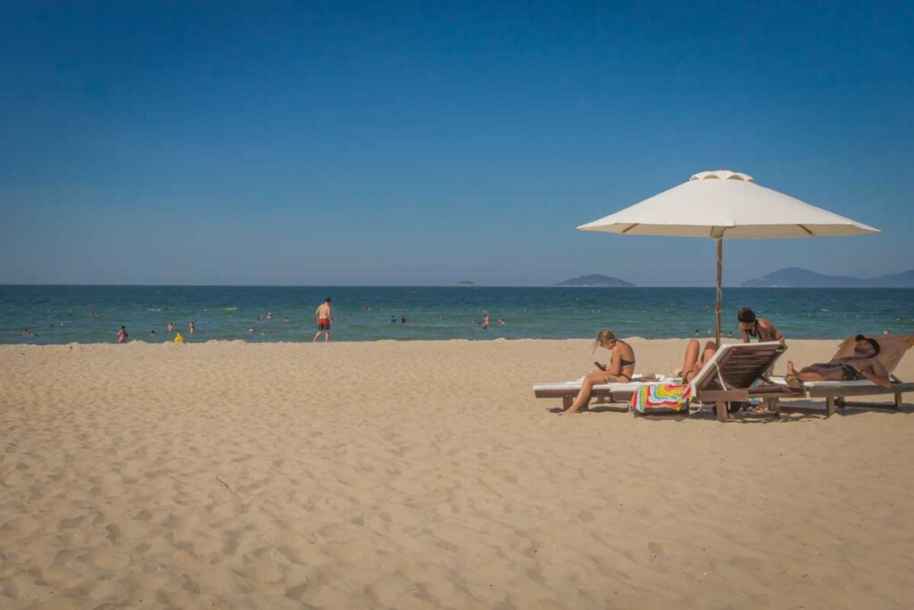 Tourists sunbathing and swimming under umbrellas on An Bang Beach in Hoi An