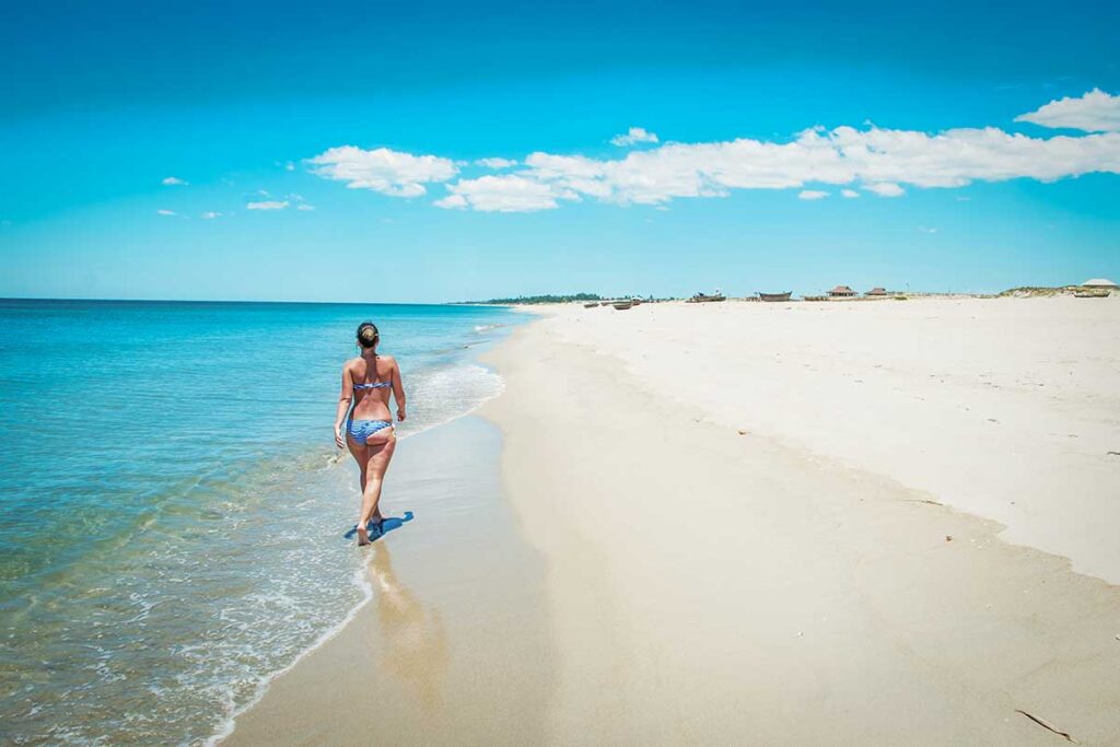 Traveler walking along the white sandy shoreline of An Bang Beach with turquoise water in Hoi An