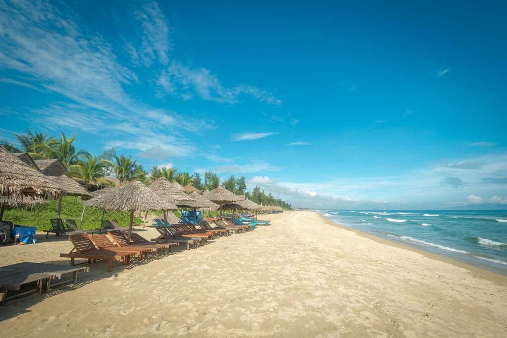 Peaceful morning view of An Bang Beach with straw parasols and empty sunbeds under a blue sky