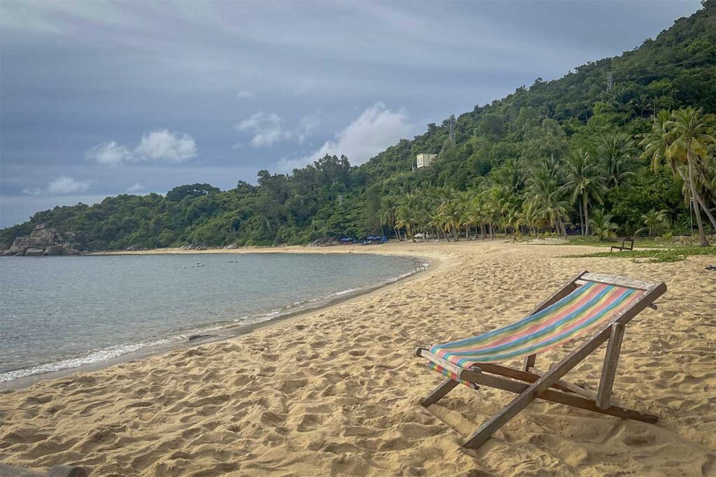 Quiet Bai Bim Beach on Cham Island with golden sand, calm waves, and forested hills in the background.