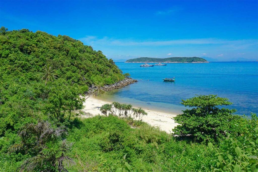 Small palm-lined Bai Huong Beach on Cham Island with fishing boats and a peaceful turquoise bay.