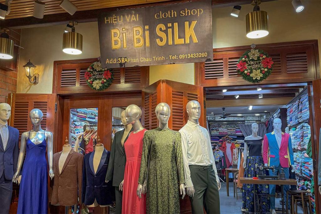 Exterior of Bi Bi Silk tailor shop in Hoi An, displaying suits and dresses made by expert local tailors specializing in tailor made clothing.