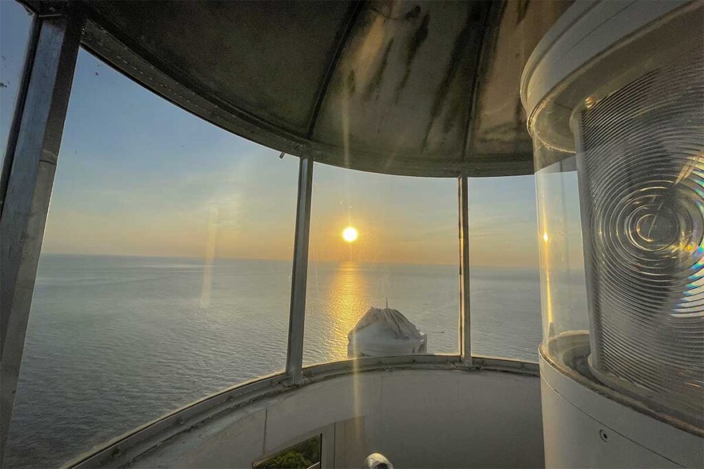 Sunset view from inside Cham Island lighthouse, looking over the calm ocean as golden light reflects on the water.