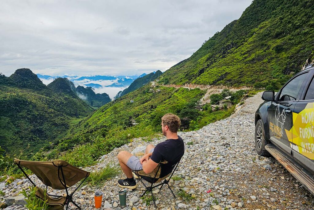 Ha Giang Loop by car - a traveler sitting in front of a car watching the stunning mountain scenery of Ha Giang