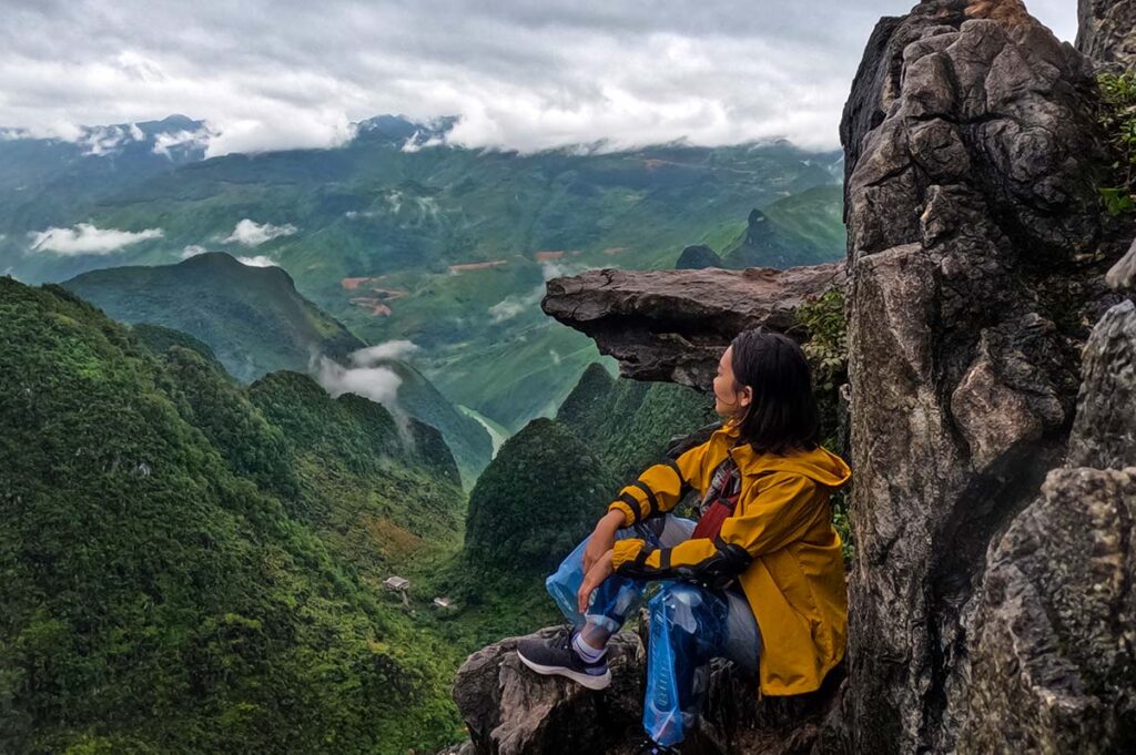 A girl sitting next to an overhanging rock, which is a popular photo stop along the Ma Pi Leng Skywalk