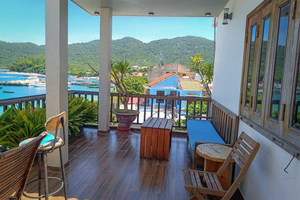 Balcony view from Monkey Homestay on Cham Island, overlooking the fishing village and harbor surrounded by green hills.