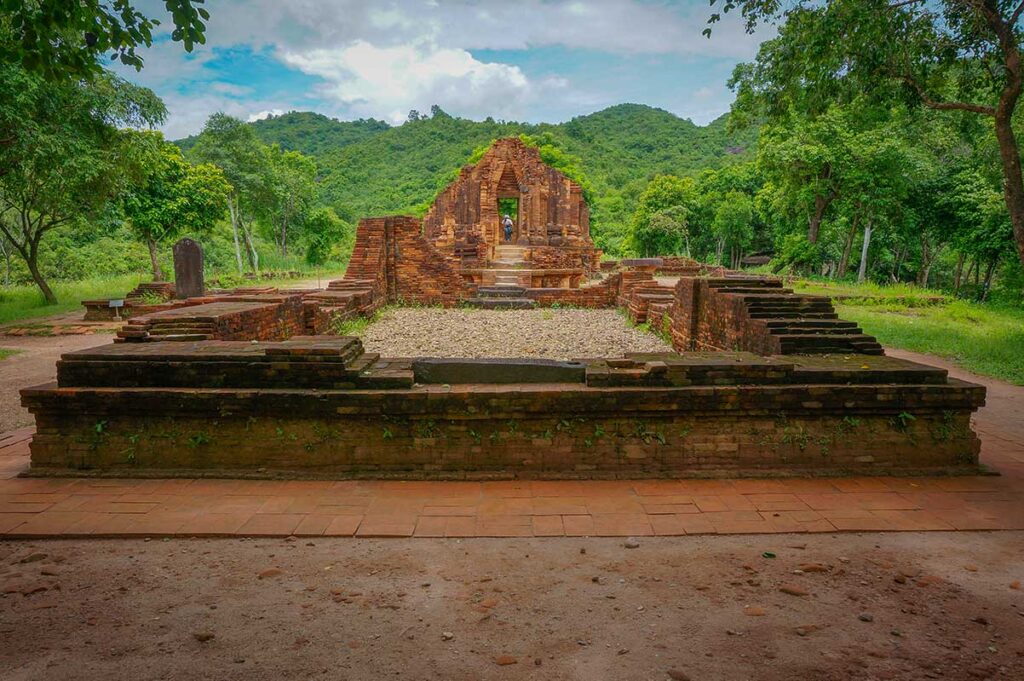 ham temple ruins at My Son Sanctuary surrounded by dense forest and hills, viewed from the base of an ancient brick platform.