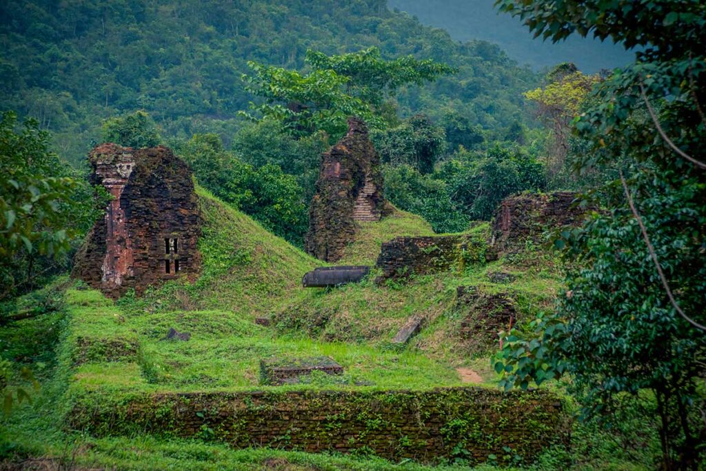 Ruins of ancient Cham temples at My Son Sanctuary covered in green vegetation, showing the peaceful jungle setting of the valley.