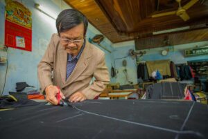 Experienced tailor in Hoi An cutting fabric for a bespoke suit, showcasing traditional techniques and attention to detail.
