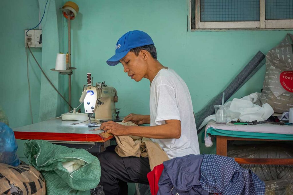 Tailor in Hoi An sewing clothing by hand in a small workshop, part of the city’s long tradition of custom made tailoring.