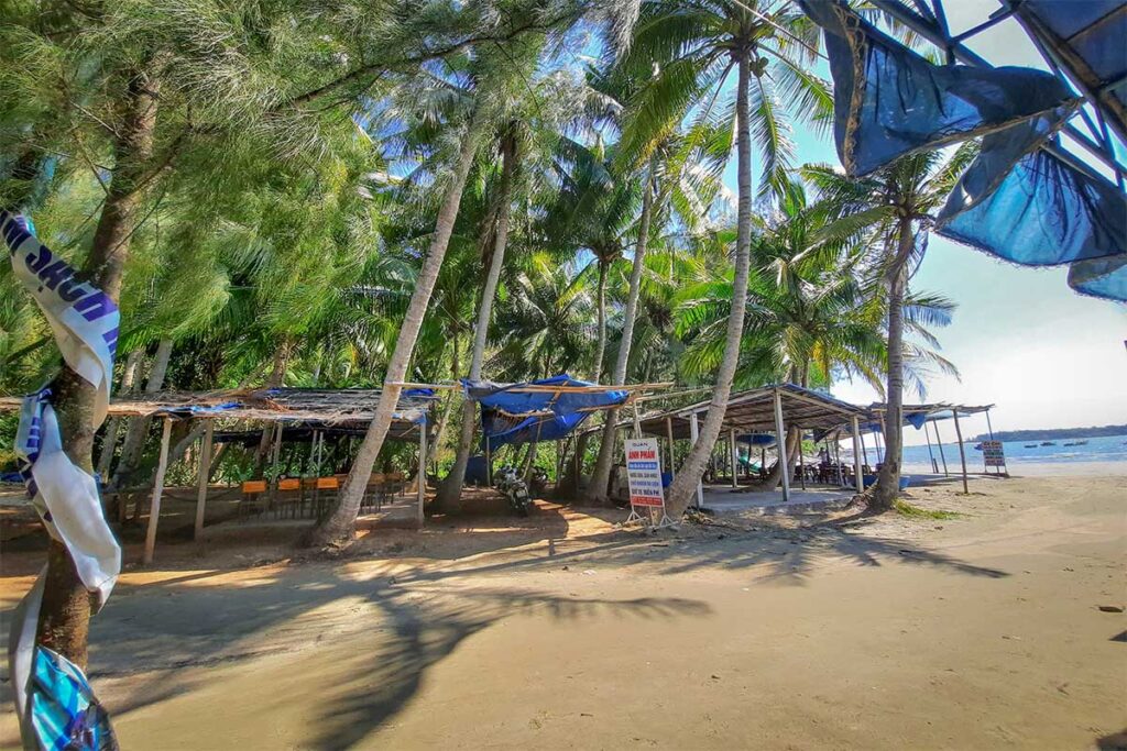 Simple beachfront shacks shaded by palm trees on Tam Hai Island, serving local seafood along the sandy shore.