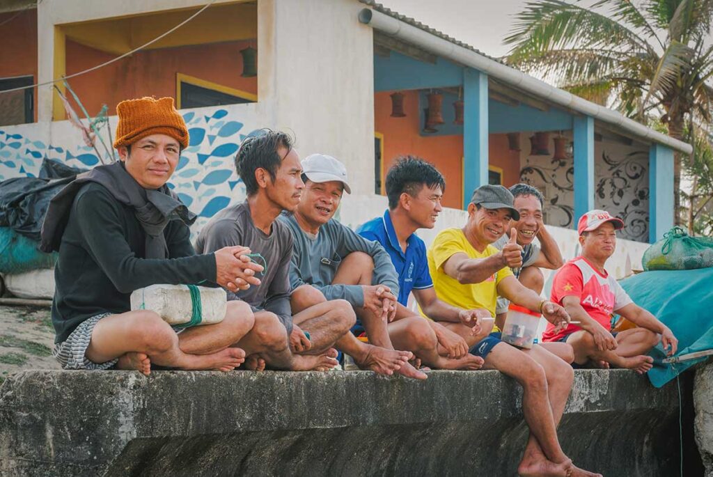 Group of local fishermen relaxing near the murals of Tam Thanh Mural Village, reflecting the friendly atmosphere and everyday coastal life of Quang Nam Province.