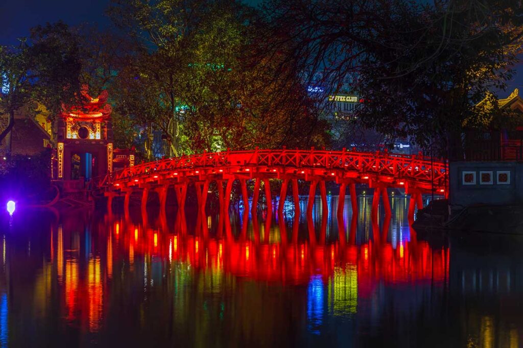 The Huc Bridge seen at night time with the lights on the bridge reflecting in the water of Hoan Kiem Lake