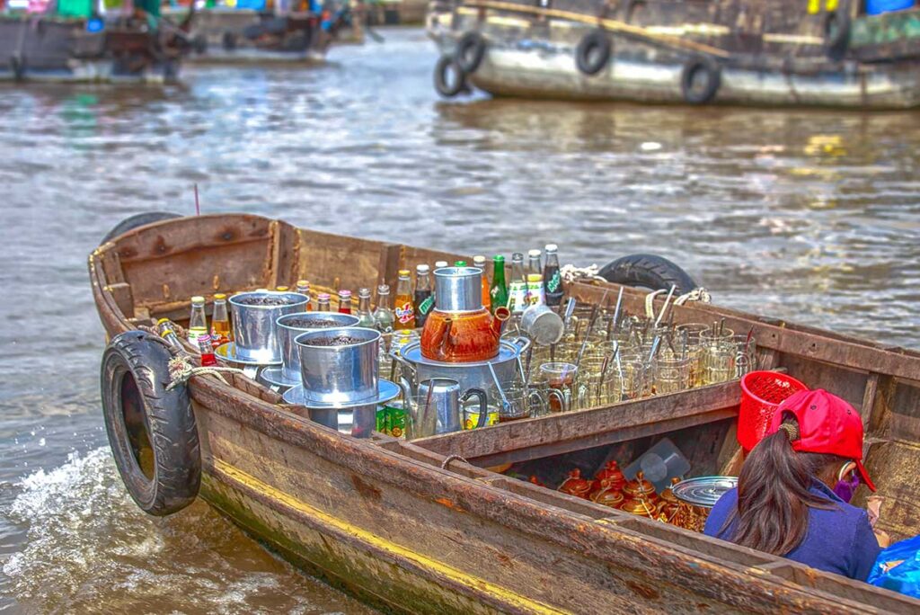 Small wooden boat serving as a floating coffee stall with bottles, glasses, and metal filters at Cai Rang Floating Market.