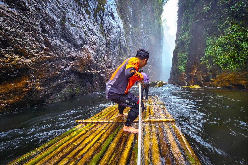 a person in a gorge on a bamboo raft dragging a rope to get closer to the Dragon Waterfall 