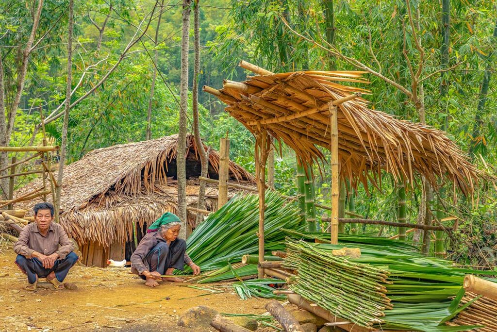 Ethnic woman and man working with bamboo and leaves to create mats in Pu Luong