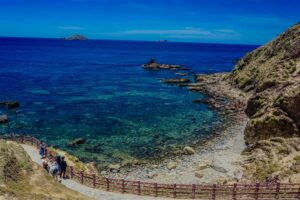 Visitors walking the boardwalk at Eo Gió overlooking rocky shores and transparent blue water