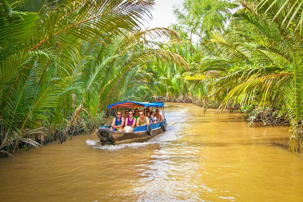 Tourist boat ride through canals in Ben Tre – Group of travelers cruising under dense nipa palms on a Mekong Delta waterway.