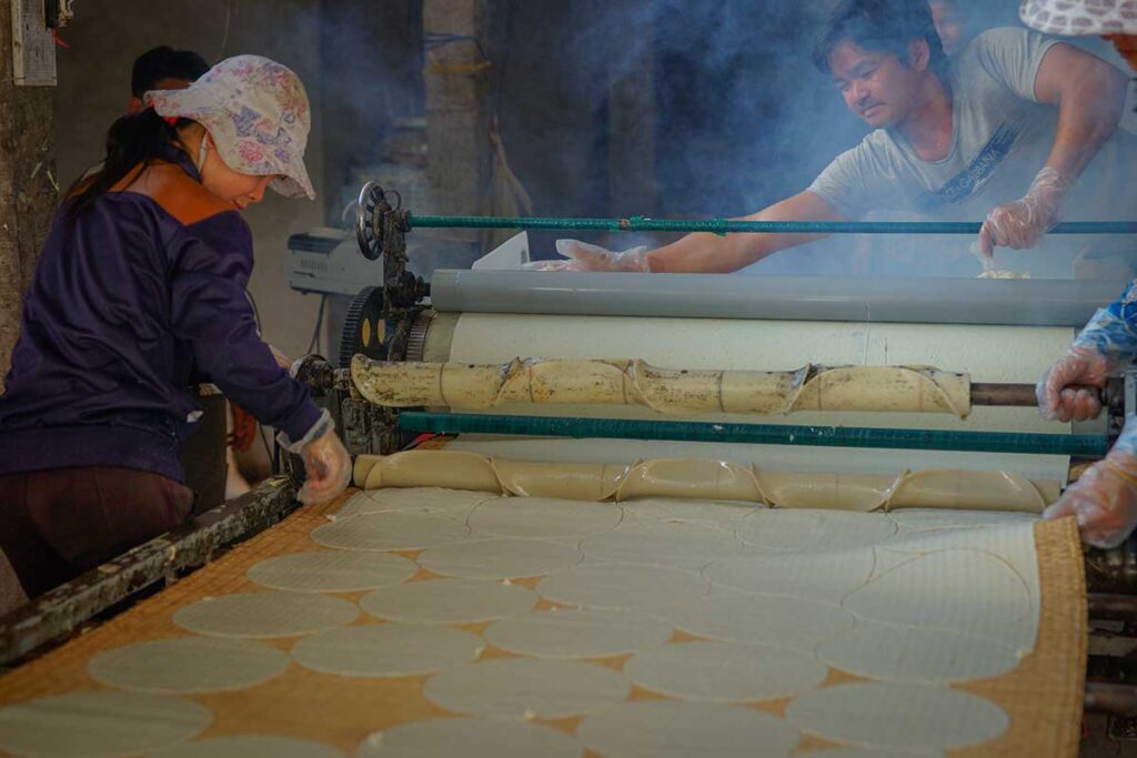 Artisans making rice paper sheets in a steaming workshop in Ben Tre, a famous Mekong Delta food tradition in Vietnam.