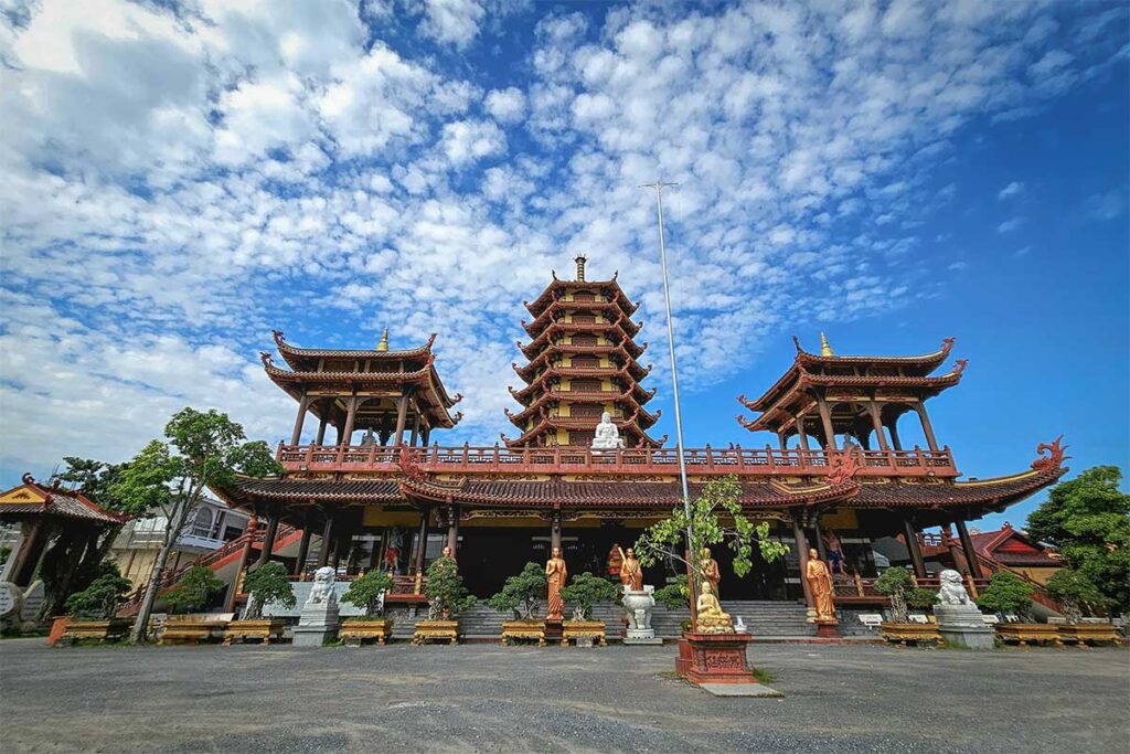 Jade Buddha Temple in Vinh Long, a modern pagoda with a tall red pagoda tower and statues set against a bright blue sky.