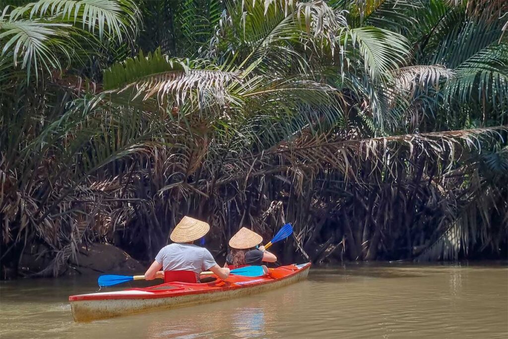 Kayaking in Ben Tre – Tourists paddling a kayak under nipa palm trees on a quiet canal in Ben Tre, Mekong Delta, Vietnam.