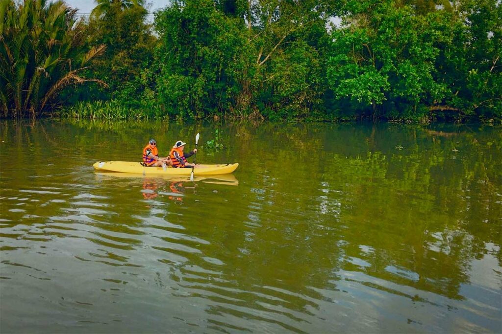 Kayaking in Can Tho, Mekong Delta – Tourists paddling a yellow kayak along a quiet river, surrounded by dense green tropical vegetation.