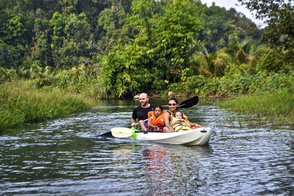 A man, woman, and child paddling a kayak along a peaceful stream, exploring the waterways of Cat Tien National Park.