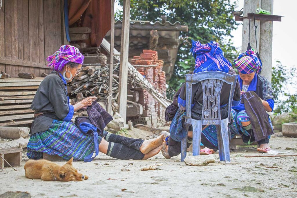Local ethnic woman in traditional clothes are sitting in front of a house in a village in Mu Cang Chai district