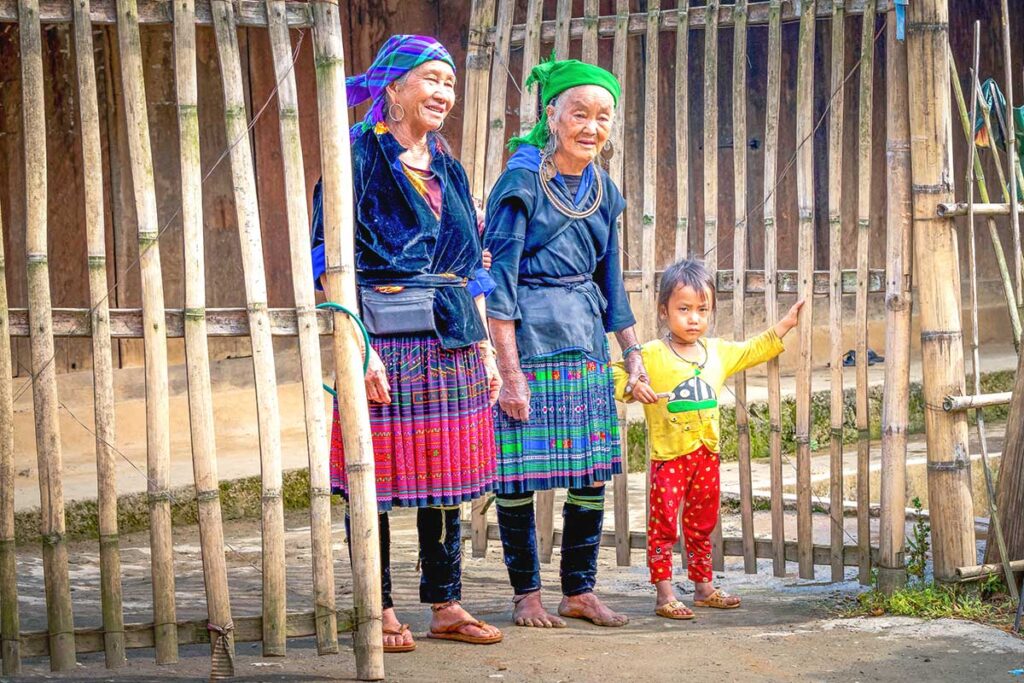 Two colorful ethnic elderly woman wearing traditional clothes and a young child in front of a local house in Mu Cang Chai