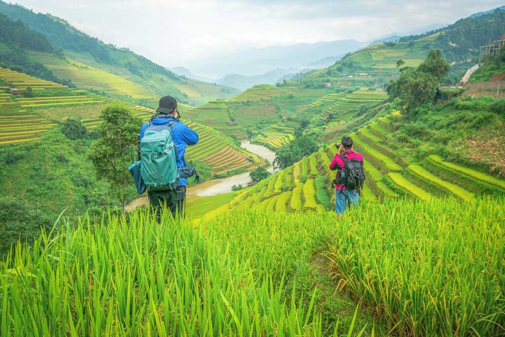 Two travellers wearing a small backpack making a trekking through the rice fields of Mu Cang Chai