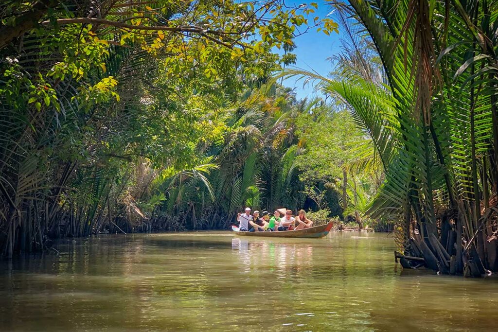 Tourists on a sampan boat tour through palm-lined canals near My Tho, Vietnam, a classic Mekong Delta experience.