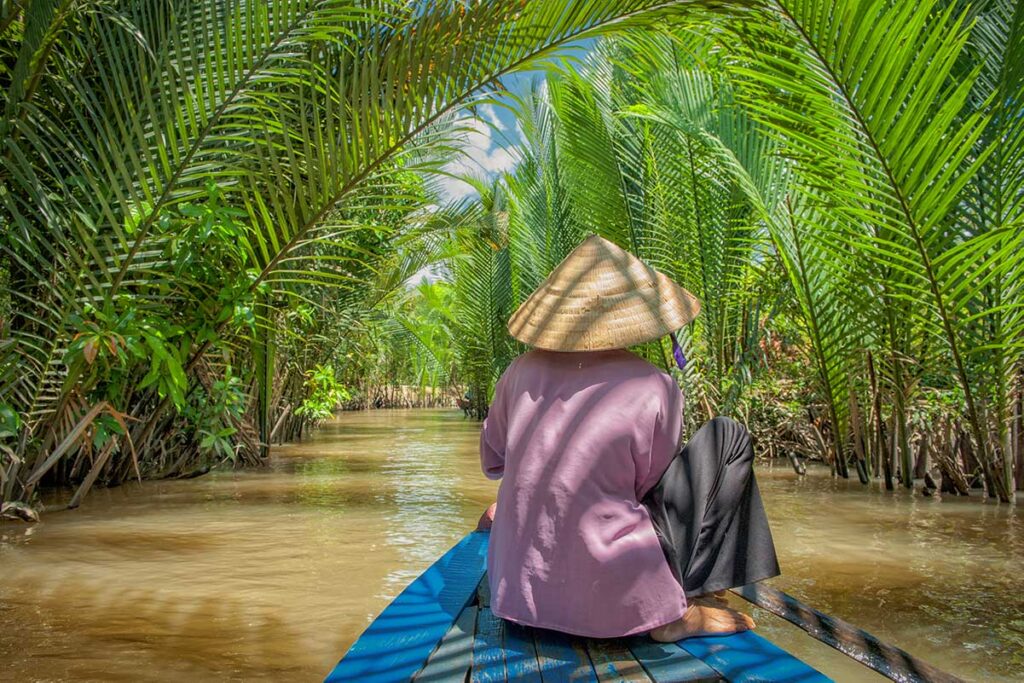 Rowing sampan through nipa palms in Vinh Long – Traditional boat ride along shaded canals lined with lush nipa palm trees in the Mekong Delta.