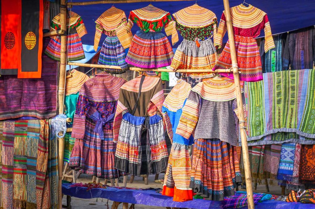Different colorful ethnic colored clothes are hanging on a stall at Bac Ha Market