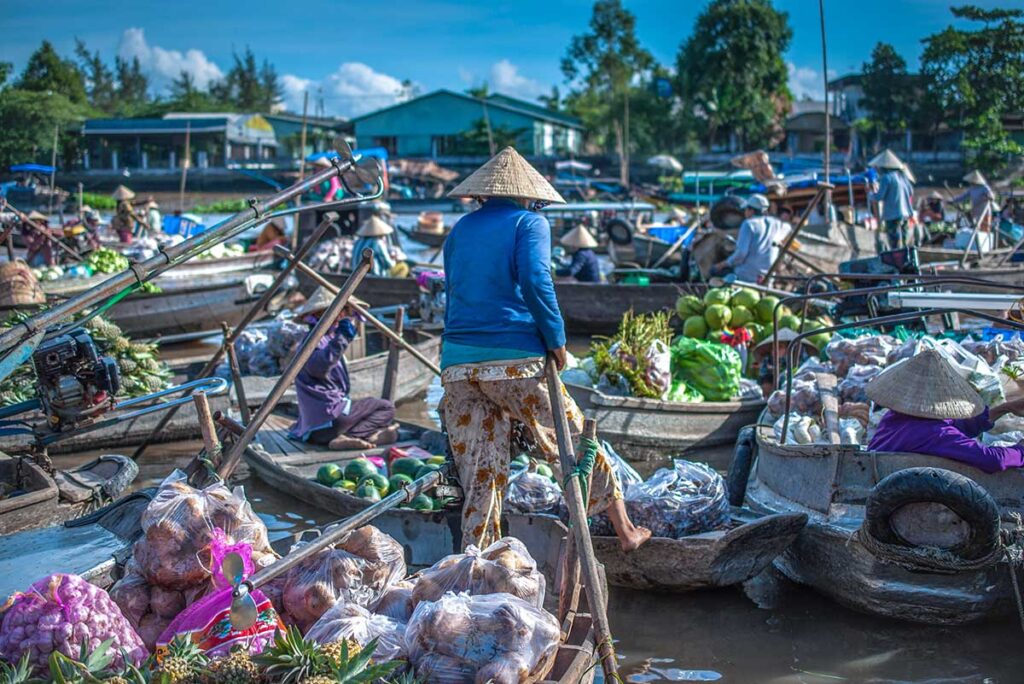 Vendors balancing on wooden boats loaded with produce at Phong Dien Floating Market in the Mekong Delta.