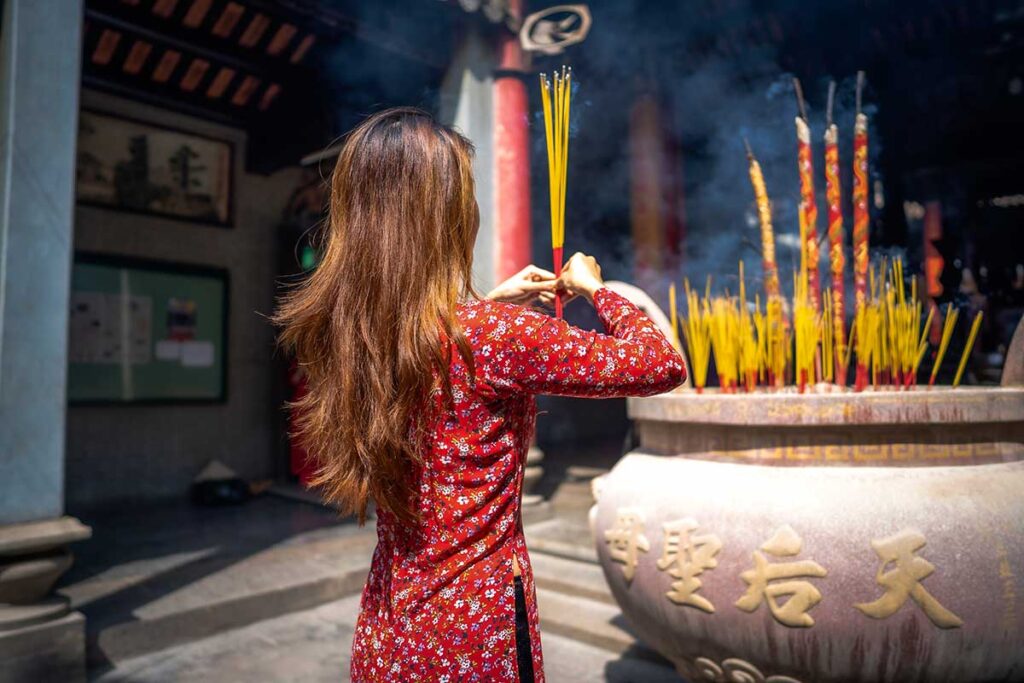 Vietnamese woman holding incense sticks while praying at a pagoda during Tet Vietnamese New Year