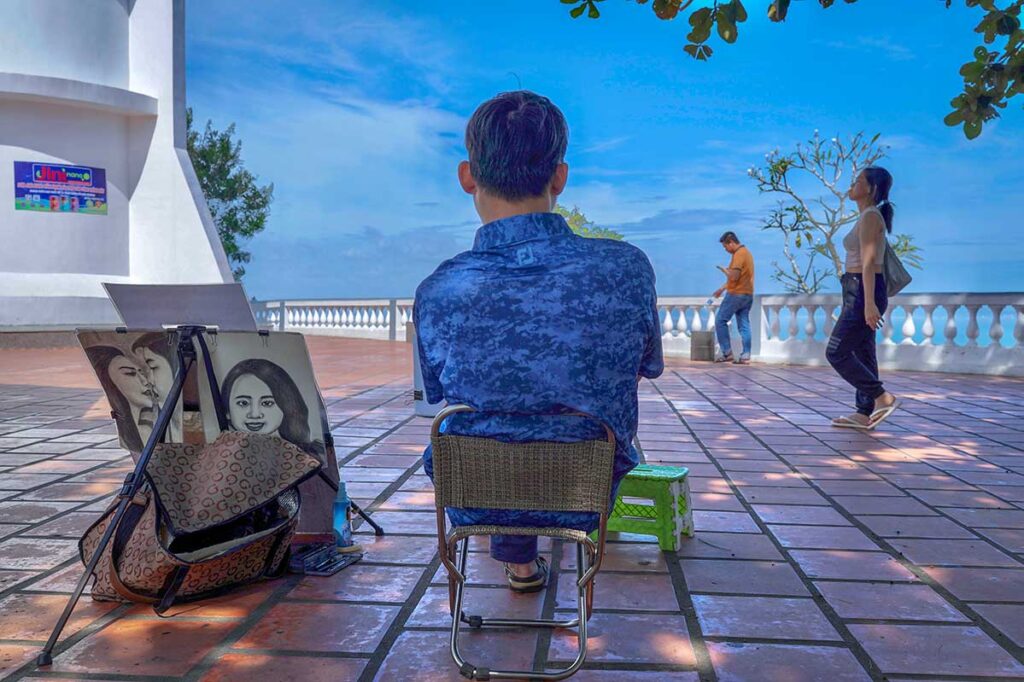 An artist is sitting at the base of Vung Tau Lighthouse waiting to draw people