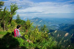 A girl with backpack is sitting on the peak of Bach Ma National Park enjoying the view