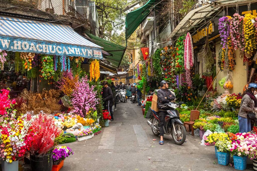 A narrow alley in Hanoi Old Quarter with people selling flowers