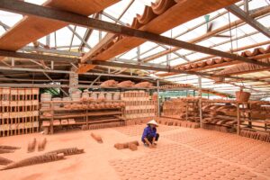 a man sitting in a warehouse full of clay pots in Bat Trang Ceramic Village near Hanoi