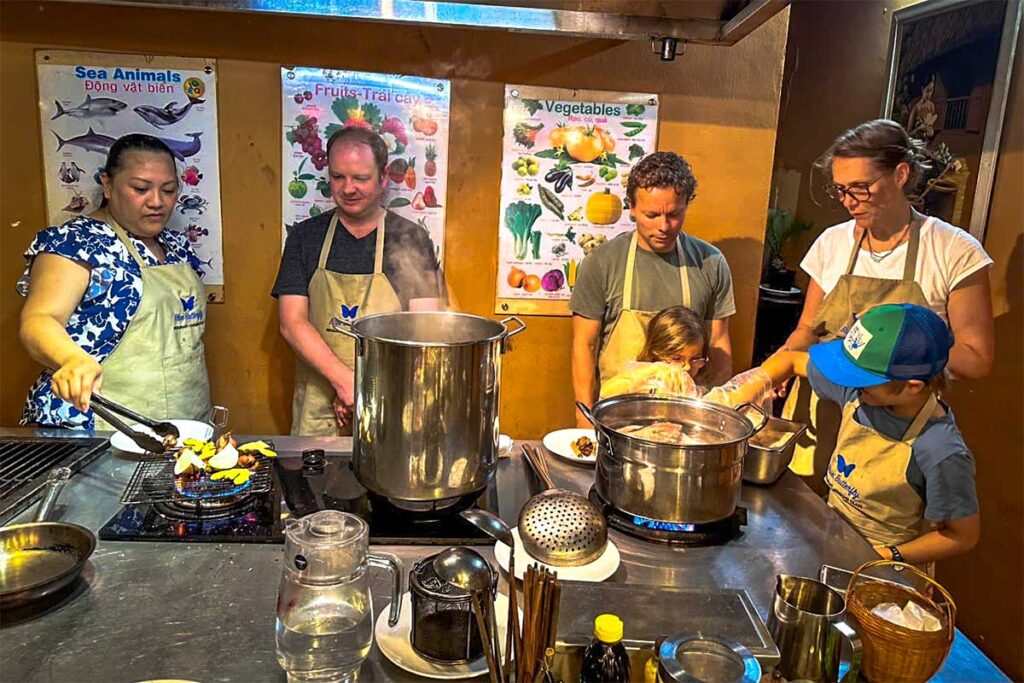 Blue Butterfly Cooking Class: A group of adults and children, all wearing aprons, engage in a fun and interactive cooking class at Blue Butterfly in Hanoi.