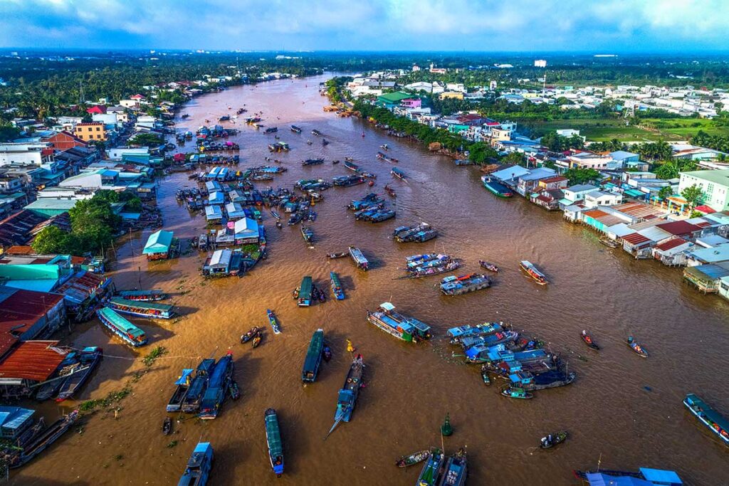 Cai Rang Floating Market Aerial View: Aerial view of the bustling Cai Rang floating market on the Mekong River, with Can Tho city's skyline visible in the distance.