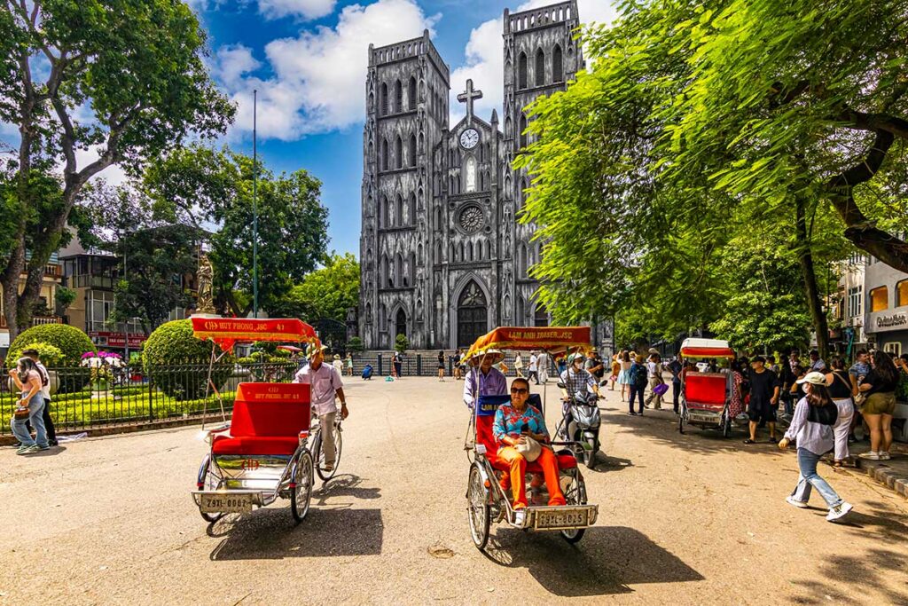 A row of colorful cyclos, traditional Vietnamese bicycle taxis, line up in front of St. Joseph's Cathedral in Hanoi, ready to take tourists on a tour of the city.