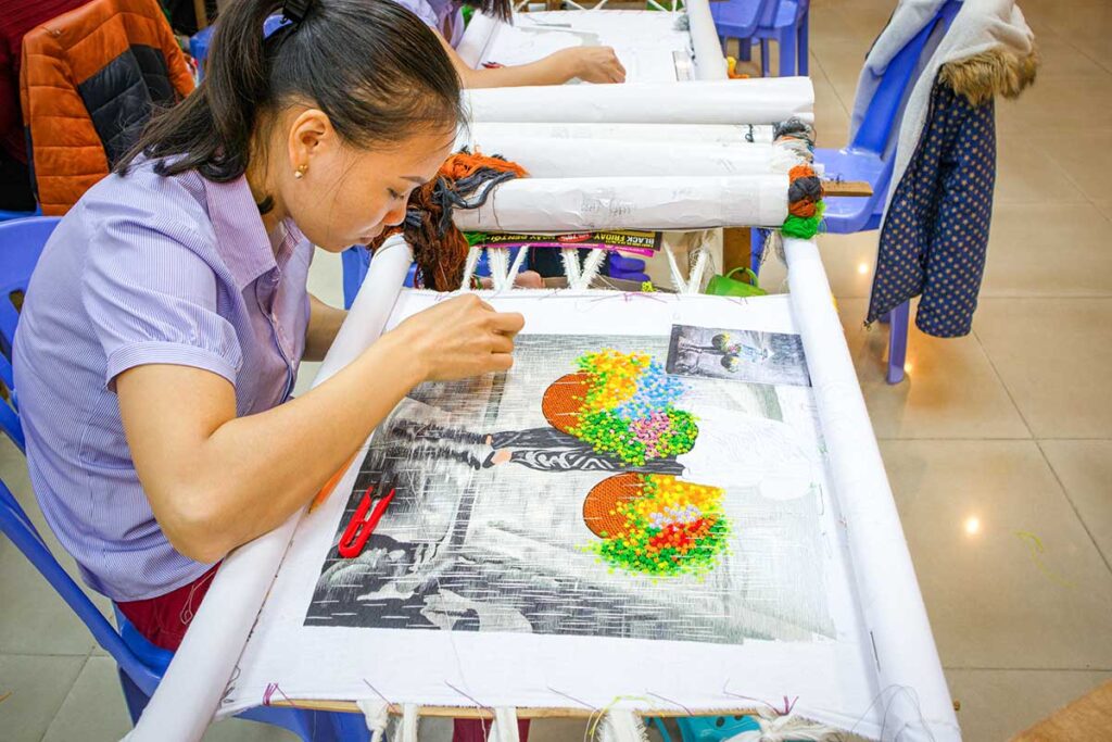 Close-up of a Vietnamese woman's hands embroidering delicate patterns in a Hanoi workshop.