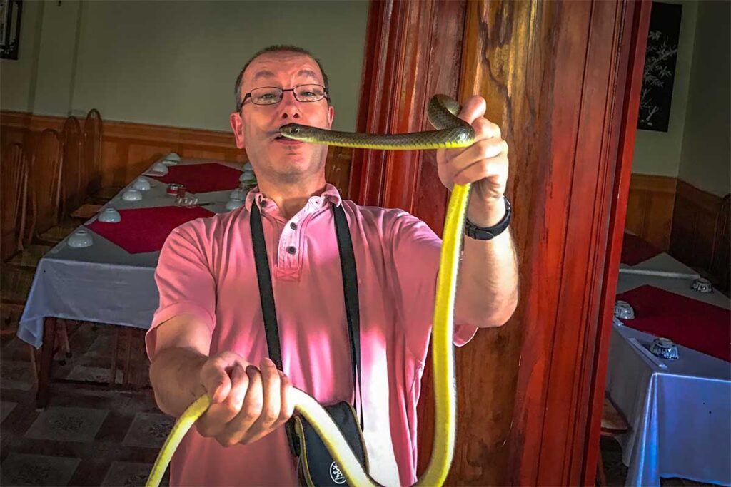 A brave tourist poses with a live snake in Le Mat Snake Village, known for its snake-handling traditions.