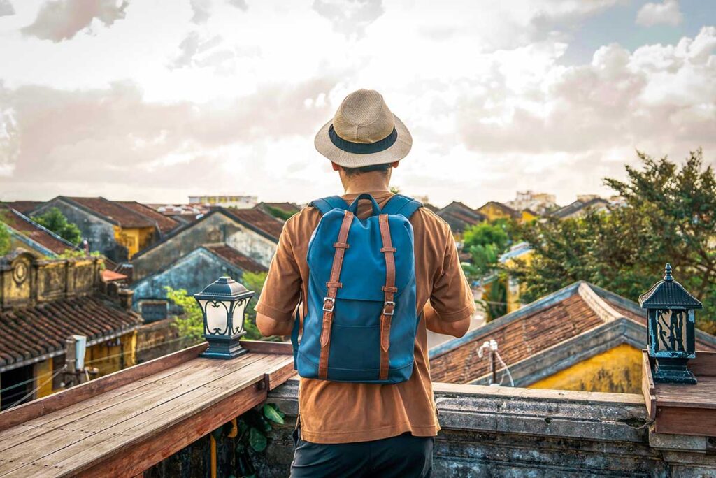 Solo male traveler with a backpack standing at a café, enjoying the view of Hoi An's rooftops