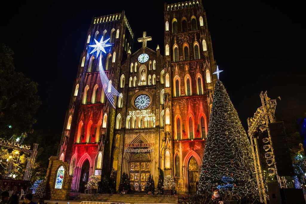 St. Joseph's Cathedral in Hanoi, Vietnam, adorned with a towering Christmas tree and twinkling lights, creating a festive atmosphere during the holiday season.